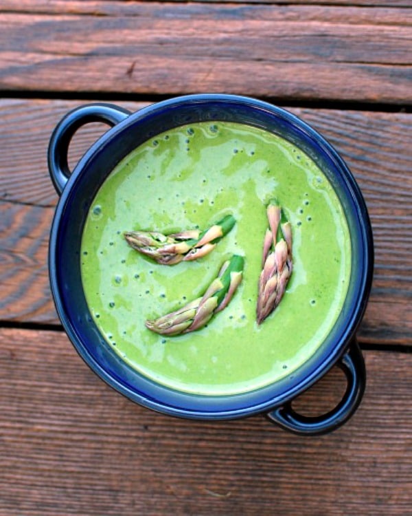 overhead view of a dark blue bowl with bright green asparagus bisque