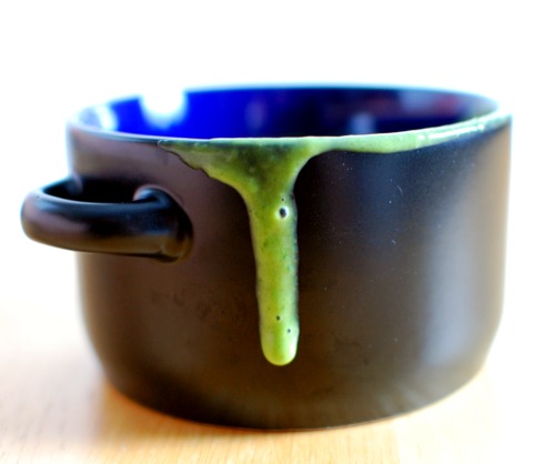 a black bowl with a bright green drip of asparagus bisque on the side.