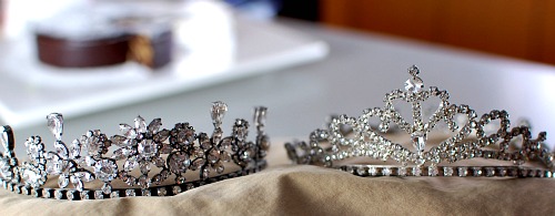 a crown and a tiara sit side by side on a tan piece of cloth.