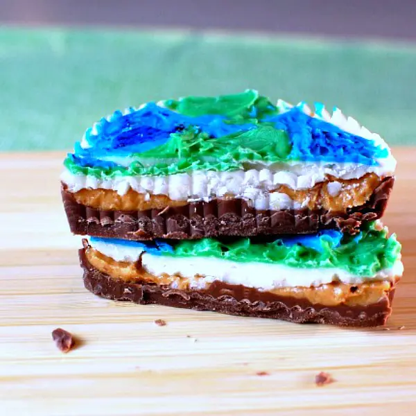 Close up of a stack of Earth Day peanut butter cups decorated with blue and green chocolate to look like earths. Cup is sliced in half to see the peanut butter middle.