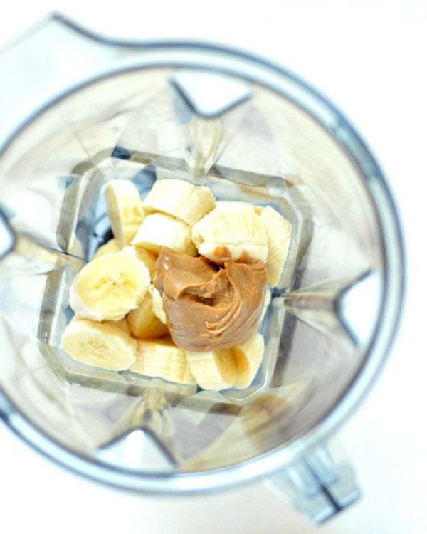 overhead view of peanut putter and sliced banana in a blender jar before blending.