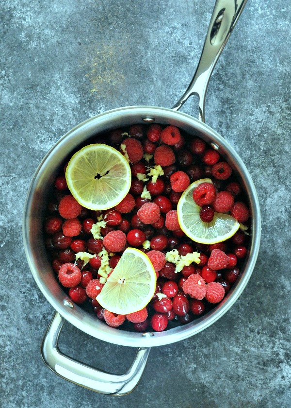 overhead view of Ginger Cranberry Sauce being made: large stainless saucepan filled with whole fresh cranberries, raspberries, lemon slices, and finely minced ginger.