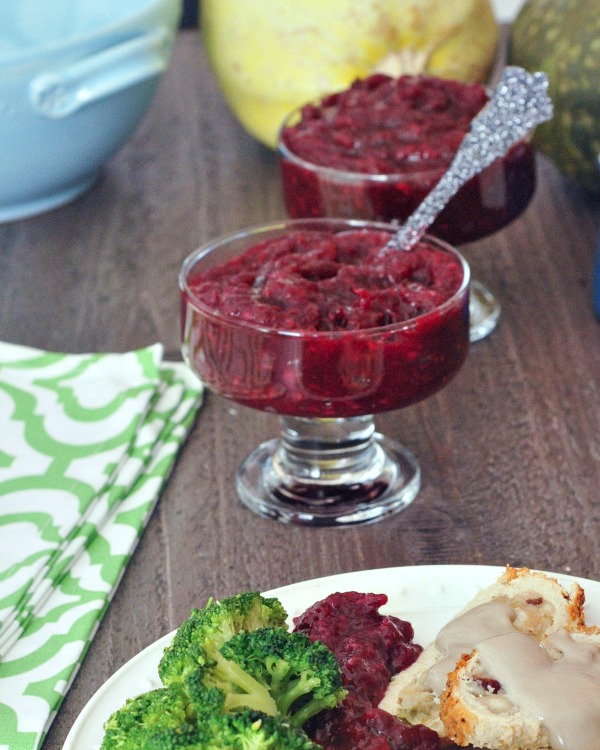 two glass serving dishes of bright red cranberry sauce in the middle of a holiday table (the edge of a dinner plate with roast, broccoli, and cranberry sauce is in view in the lower corner of the photo)