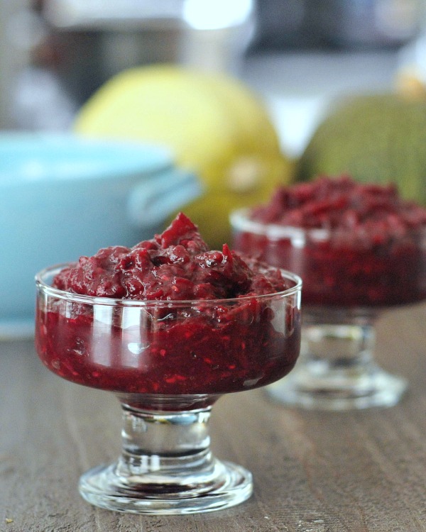 two small glass serving dishes of Ginger Cranberry Sauce on a wooden table. blurred in background: serving bowls and whole spaghetti squash