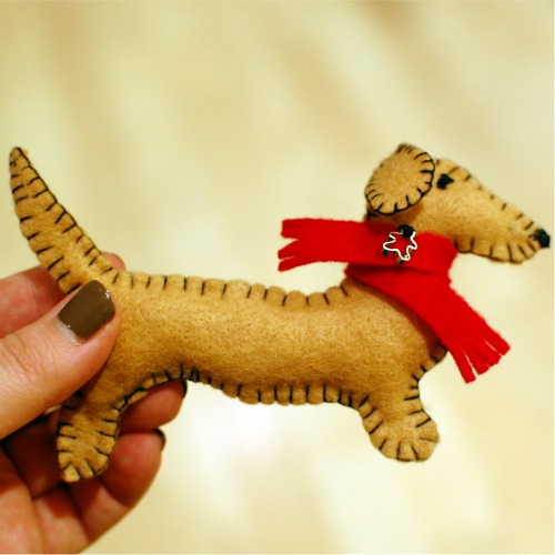 A hand holding a finished handmade dachshund ornament.