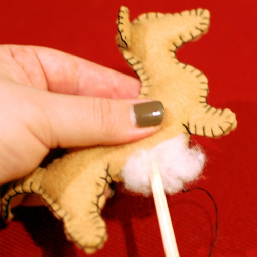 Handmade felt dachshund ornament being filled with white fluffy stuffing. A chopstick is used to poke the stuffing into the head and legs evenly.