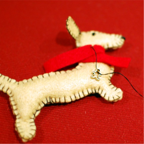 Sewing a scarf and a small silver charm onto the felt dachshund holiday ornament.