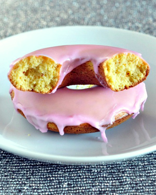 pink iced saffron donuts on a white plate, sliced in half to show yellow cake inside