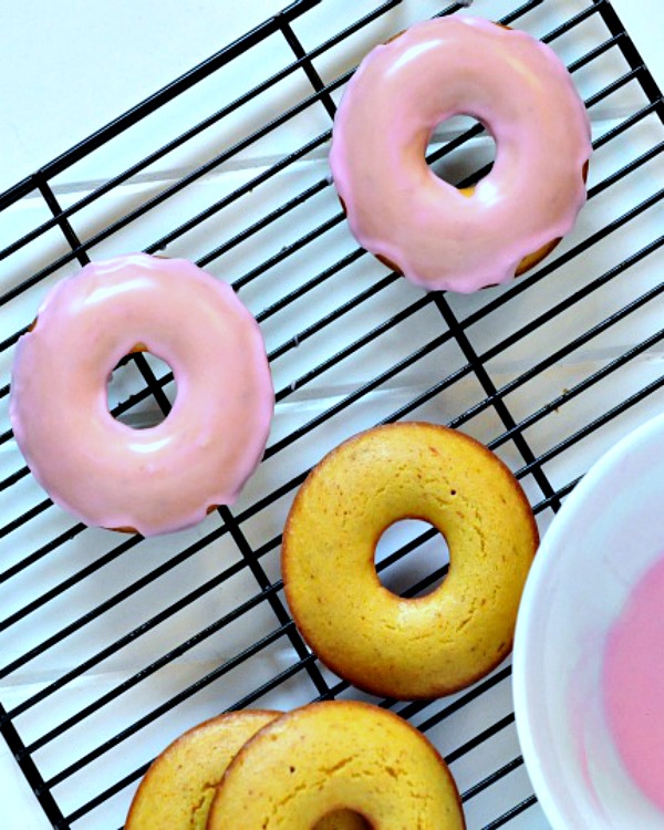 overhead view of pink iced saffron donuts on a baking rack, bowl of pink rosewater icing on the side