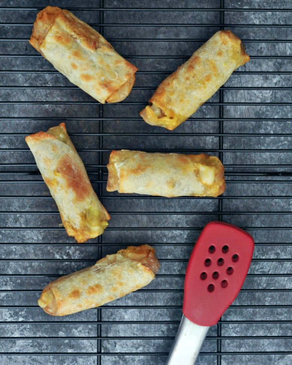 reuben rolls (jackfruit reuben sandwich filling wrapped in egg roll wrapper) cooling on a wire rack, a pair of red tongs on side.