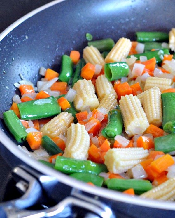 sautéed vegetables in a skillet for fried rice: diced onion, pea shoots, baby corn, diced carrot