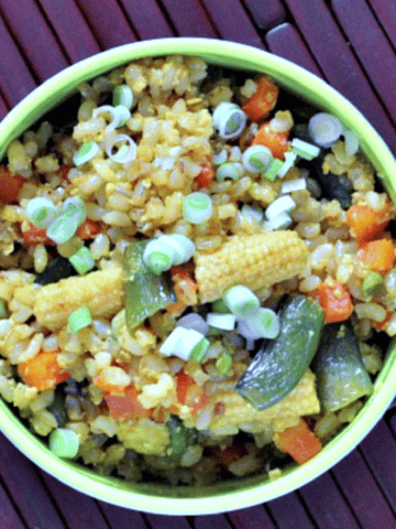 overhead view of vegetable fried rice in bowl: pea shoots, baby corn, diced carrot, golden fried rice
