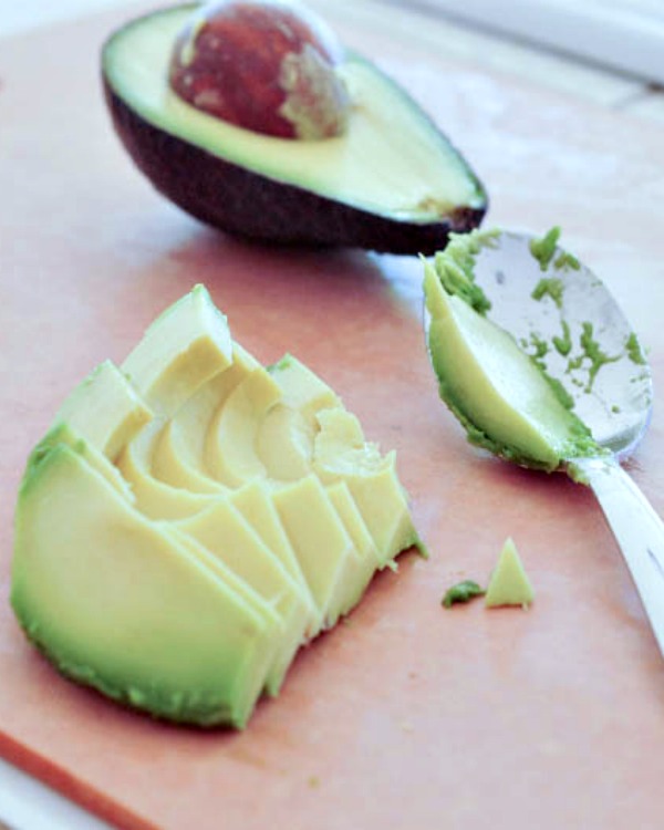 avocado slices on a board, other half avocado still in peel with seed