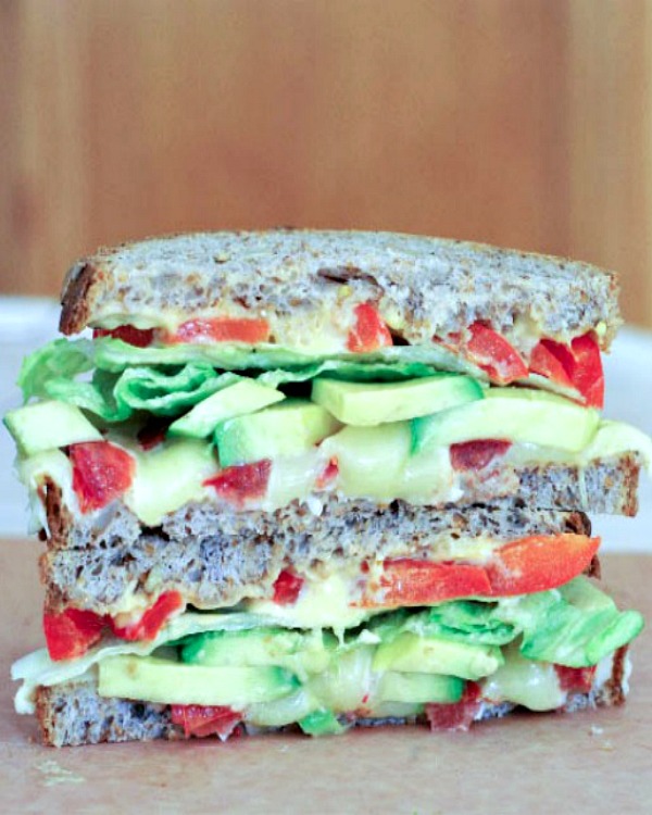 side view of a fresh vegetable grilled cheese sandwich with avocado, tomatoes, lettuce, one half stacked on top of other half.