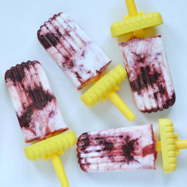 Cherry cheesecake popsicles with shortcake crumb on bright yellow handles on a white ceramic platter