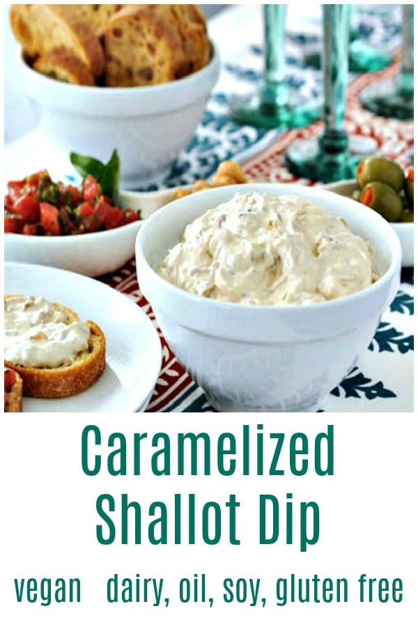 a white serving bowl of caramelized shallot dip, with toasted baguette slices, a bowl of olives, and green stemmed wine glasses in background