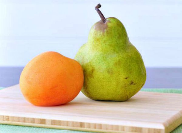 one whole apricot and one whole pear fruit on a light tan bamboo cutting board
