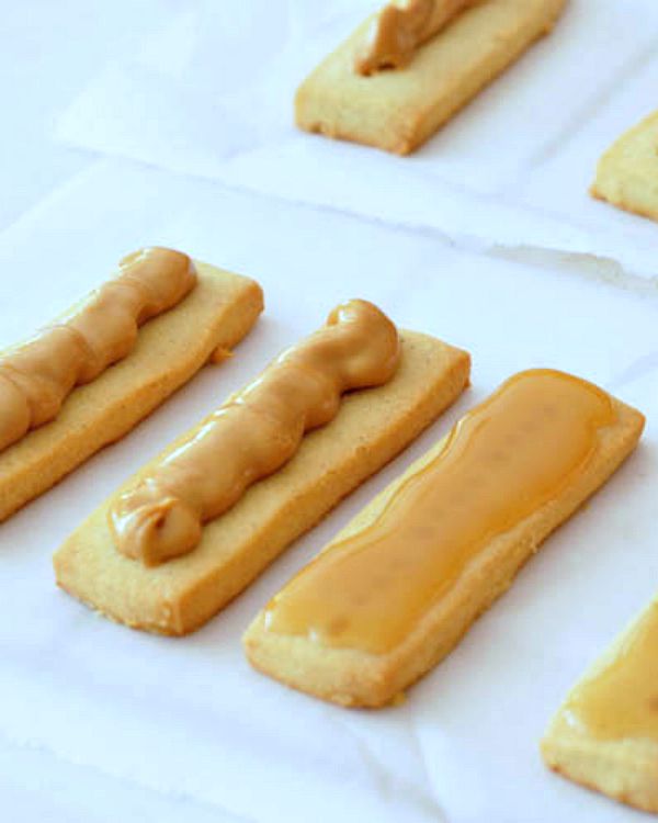 How To Make Vegan Twix: shortbread cookies topped with caramel or peanut butter, lined up on parchment