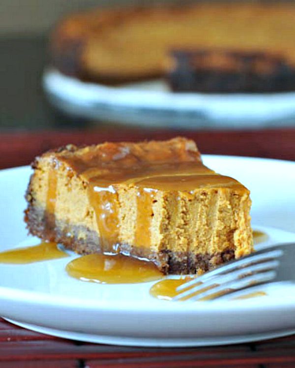 one forkful out of a slice of pumpkin cheesecake on a white plate; the remaining whole cheesecake in background.