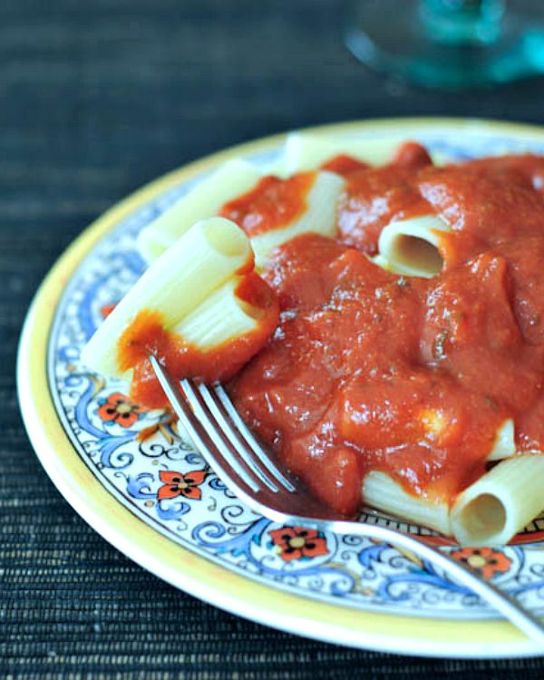 A traditional blue, yellow, and white Italian decorated plate with noodles and marinara sauce.