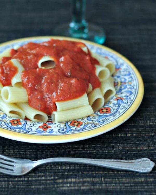 A traditional blue, yellow, and white Italian decorated plate with noodles and marinara sauce.