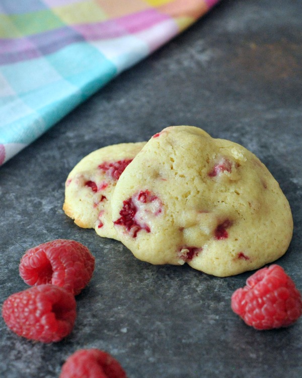 Raspberry Lemon Cheesecake Cookies stacked three high, with fresh raspberries scattered about