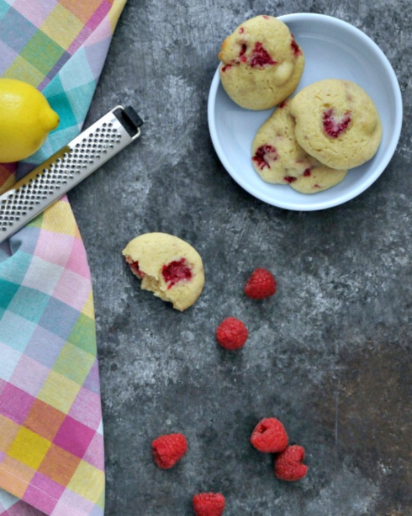 Raspberry Lemon Cheesecake Cookies on a plate, fresh raspberries, a lemon and zester nearby