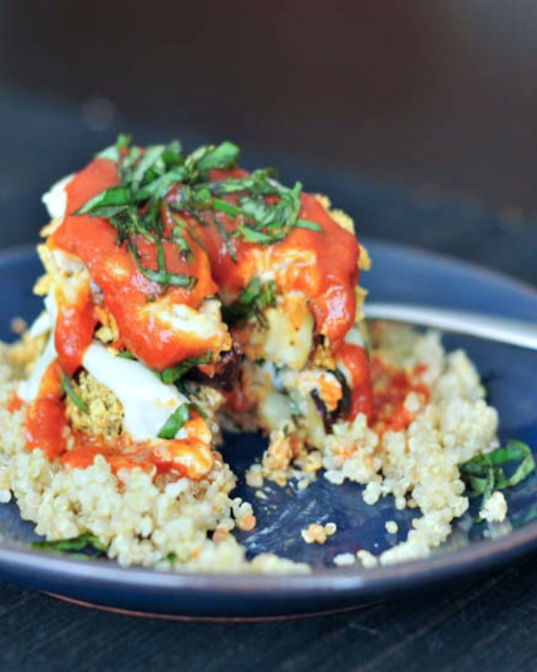 two slices of crispy eggplant stacked on top of quinoa and covered with marinara sauce and fresh chopped basil leaves. a bite has been taken from the dish, and a fork sits on the side of the plate.