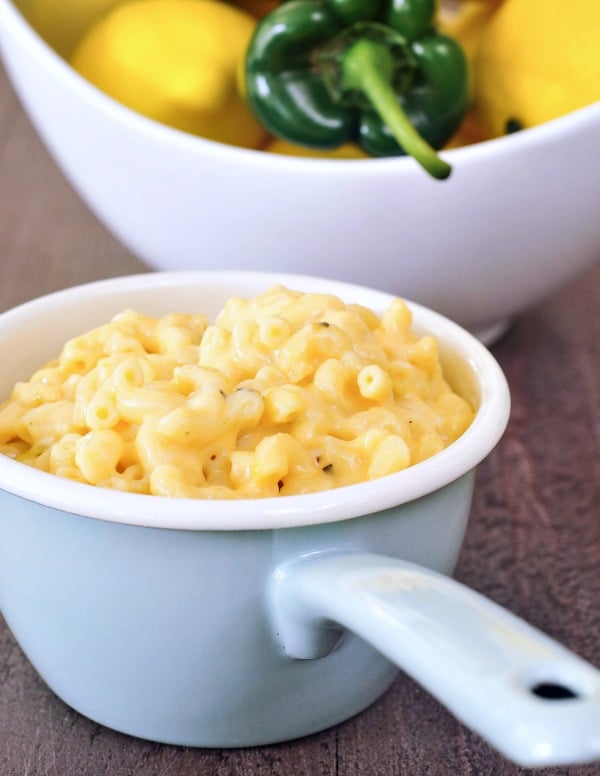 Lemon Poblano Mac and Cheese served in a light blue bowl with a handle, white bowl with lemons and a poblano in background.