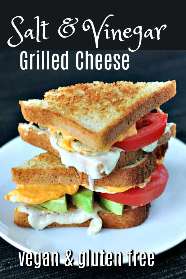 Salt and vinegar grilled cheese with avocado, tomato, potato chips against a black background, stacked on a white plate