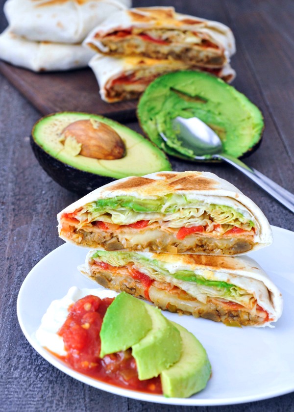 vegan crunchwrap supreme on a plate, sliced in half with avocado and salsa on the side