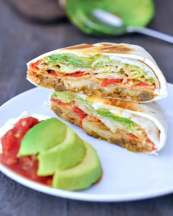 vegan crunchwrap supreme sliced in half to show inside: beans, cheese, salsa, lettuce, avocado 