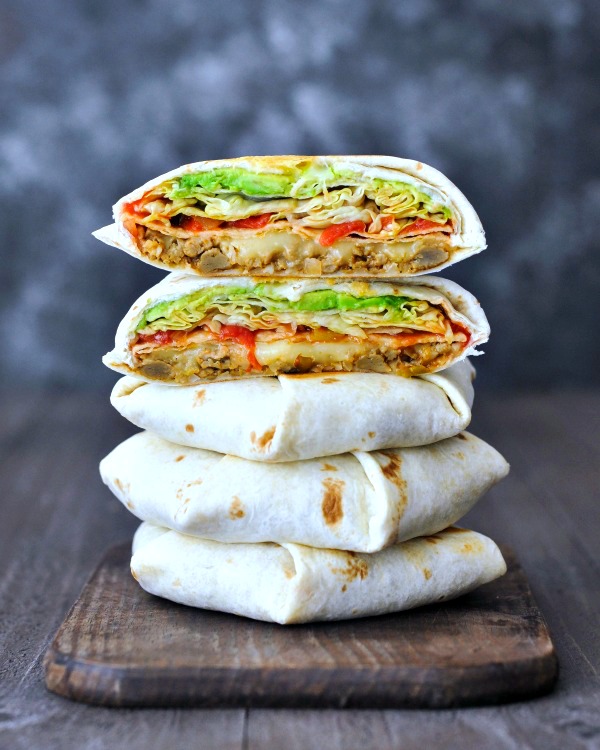 Homemade vegan crunchwrap supreme sliced in half to show filling and stacked five layers high (two halves on top of three whole crunchwraps). filling is beans, cheese, crunchy tortilla, red peppers, salsa, iceberg lettuce.