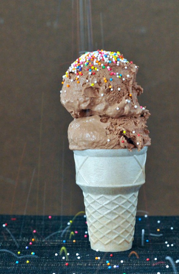 two scoops of Chocolate Oat Milk Ice Cream in a cone, being sprinkled with sprinkles