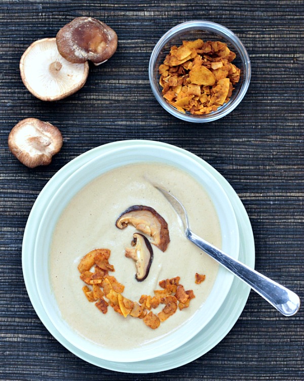 overhead view of Hearty Roasted Mushroom Bisque in a bowl, fresh mushrooms and coconut bacon on the side