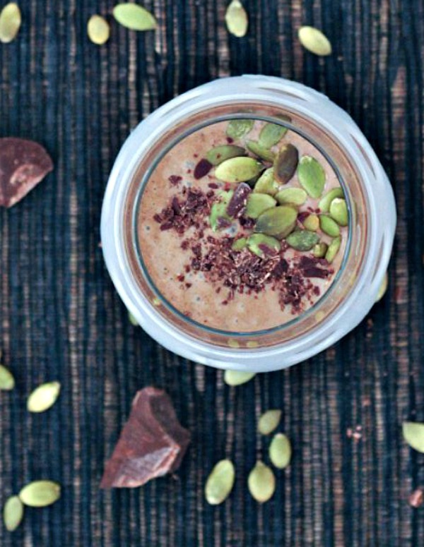 overhead view of chocolate smoothie with in a glass with a white silicone sleeve, garnished with pepitas and shaved chocolate