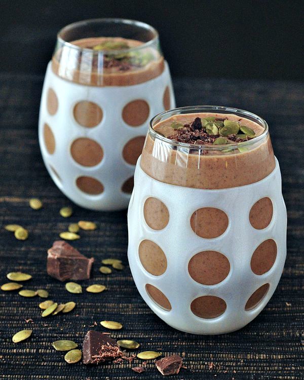 chocolate smoothie with in a glass with a white silicone sleeve, garnished with pepitas and shaved chocolate