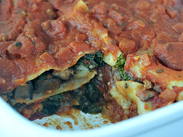 Hearty portobello kale lasagna with red sauce in a white baking dish.