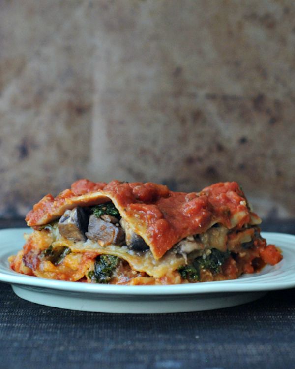Hearty portobello kale lasagna with red sauce on a white plate.