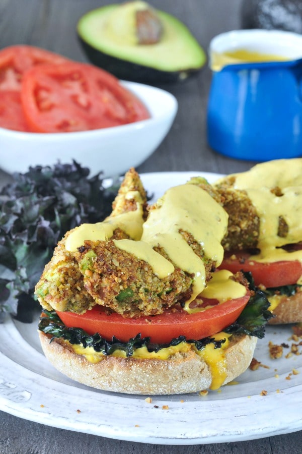 Avocado Kale Florentine - fried avocado slices with tomato and kale on an English muffin half, hollandaise sauce on top