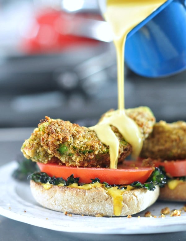 Avocado kale florentine on a rustic white dish: fried avocado slices with tomato and kale on an English muffin half, hollandaise sauce poured over top