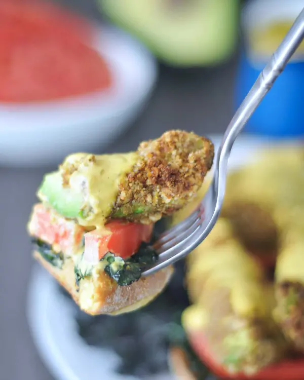 bite of Avocado Kale Florentine on a fork: piece of English muffin, tomato slice, kale, piece of fried avocado