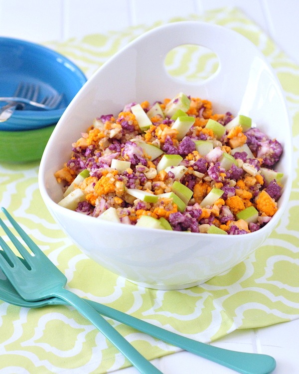 Cauliflower cashew confetti salad in a bright white serving bowl - this salad has purple, orange, and white cauliflower chopped small, with diced apple and a lemon sumac dressing