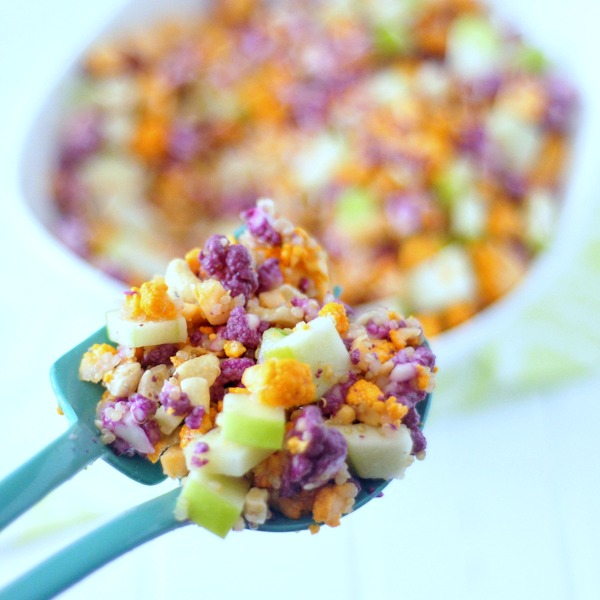 a scoop of cauliflower cashew confetti salad in a bright teal serving fork and spoon - this salad has purple, orange, and white cauliflower chopped small, with diced apple and a lemon sumac dressing