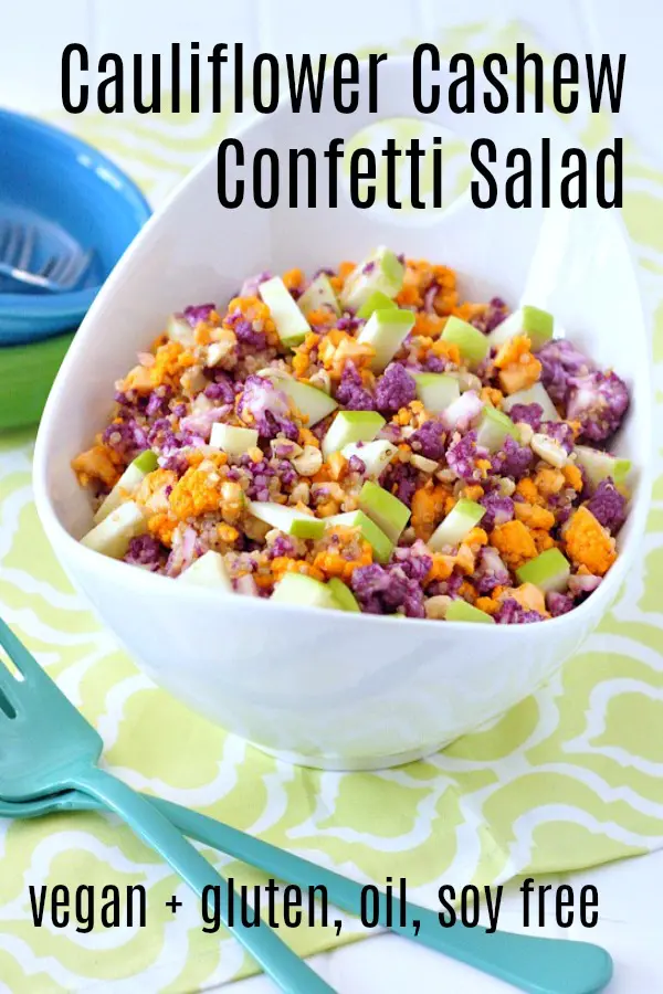 Cauliflower cashew confetti salad in a bright white serving bowl - this salad has purple, orange, and white cauliflower chopped small, with diced apple and a lemon sumac dressing