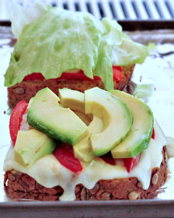 Two slices of toast with melted cheese, tomato slices, avocado slices, and iceberg lettuce.
