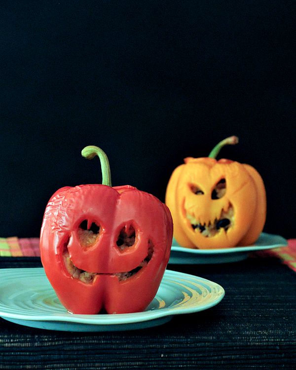 Chipotle coconut tofu filling stuffed into bell peppers carved to look like Halloween jack o lanterns, sitting on green plates against a completely black background.