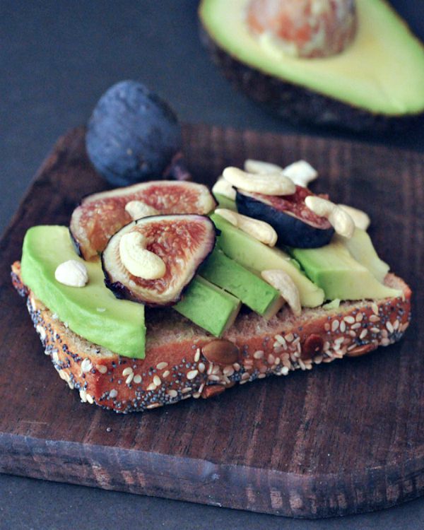 Whole grain toast topped with avocado slices, cashew pieces, and fresh figs.