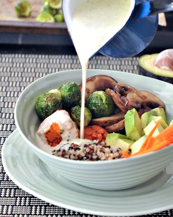 ranch dressing poured into a Buffalo Ranch Veggie Bowl served in a light blue bowl and dish: quinoa, raw carrots, avocado cubes, sautéed mushrooms, Brussels sprouts, and vegan chicken 