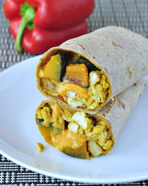 One cheesy kabocha breakfast burrito on a white plate, sliced in half to show filling (kabocha squash, vegan eggs, melty dairy free cheese).